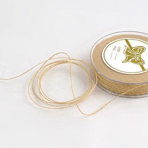 May include: A spool of natural-colored twine with a clear plastic container. The twine is wound neatly inside the container and also unwound in a loose coil. The label features a bow graphic.