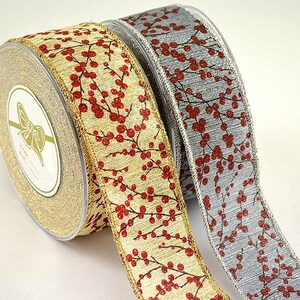 May include: Two rolls of decorative ribbon. One roll is gold with a red berry pattern, and the other is silver with the same red berry pattern. The ribbon is likely used for gift wrapping or crafting.