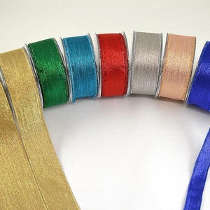 May include: A selection of colorful ribbon spools in gold, green, teal, red, silver, rose gold, and blue. The ribbons have a textured, shimmering appearance, ideal for crafts, gift wrapping, or decorative purposes.