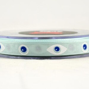 May include: A spool of light blue ribbon with a repeating pattern of white and blue eye designs. The ribbon is wrapped around a clear plastic spool, suitable for crafts and gift wrapping.