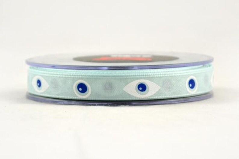 May include: A spool of light blue ribbon with a repeating pattern of white and blue eye designs. The ribbon is wrapped around a clear plastic spool, suitable for crafts and gift wrapping.