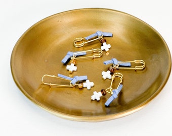 May include: Five gold safety pins with blue ribbon bows and white cross charms. Each charm has a brown bead attached.