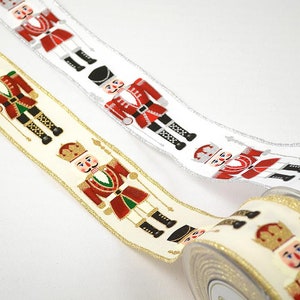 Puede incluir: Dos rollos de cinta navideña con un patrón repetido de soldados cascanueces en rojo, dorado y negro sobre un fondo blanco y crema.