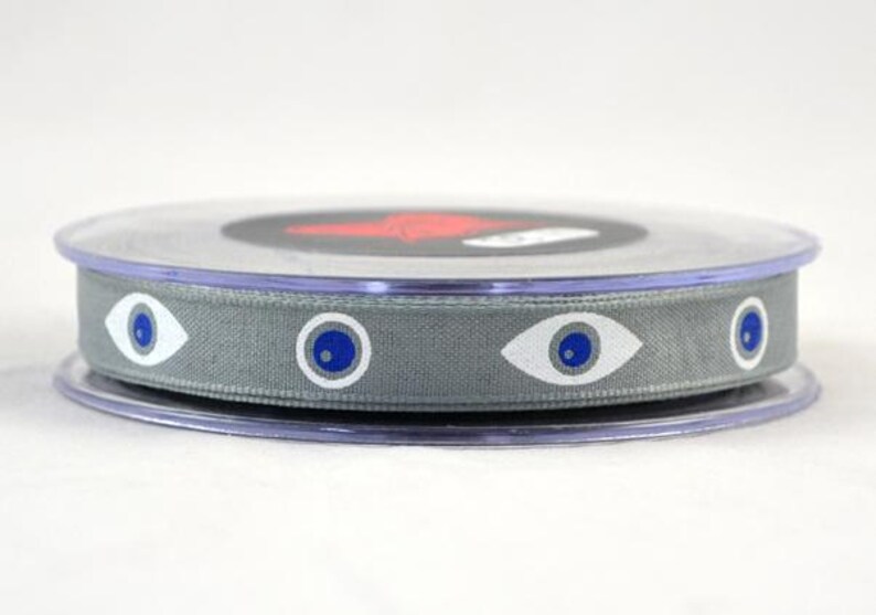 May include: A spool of gray ribbon with a repeating eye pattern in white and blue. The ribbon is wound on a clear plastic spool with a black and red design on top.