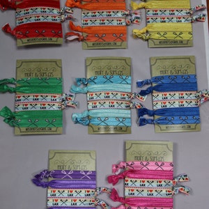 May include: Set of ten colorful hair scrunchies with a lacrosse theme. The scrunchies are made of elastic fabric and have a printed design with lacrosse sticks and the words "I Love Lax". The scrunchies are packaged on individual cards with the name "Molly & Sophia's" and an email address.