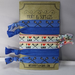 May include: A set of six blue and white lacrosse-themed hair ties. The hair ties are packaged on a brown card with the text "molly & sophia's" and "mosoknots@gmail.com".