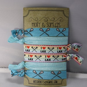 May include: A set of six blue and white lacrosse-themed hair ties with the text "I love LAX" on two of the ties. The hair ties are packaged on a brown card with the text "molly & sophia's" and "MOSOKNOTS@GMAIL.COM".