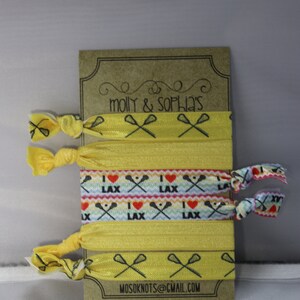 May include: A set of six yellow hair ties with lacrosse stick and heart designs. The hair ties are packaged on a brown card with the text "molly & sophia's" and "mosoknots@gmail.com".