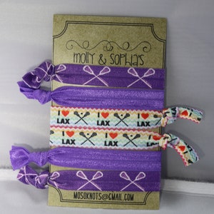 May include: Set of six purple elastic hair ties with lacrosse stick designs. Two hair ties feature a white lacrosse stick design on a purple background. Two hair ties feature a rainbow design with the words "I love LAX" and a white lacrosse stick design. Two hair ties feature a white lacrosse stick design on a purple background with white polka dots. The card reads "molly & sophia's" and "mosoknots@gmail.com".