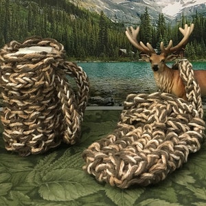 May include: Two crocheted brown and white mug cozies. One cozy is wrapped around a mug, the other is lying flat. The cozies are made with a thick, chunky yarn.