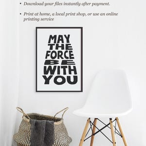 May include: A black and white printable poster with the text "May the Force Be With You" in a bold, blocky font. The poster is framed and hanging on a white wall.