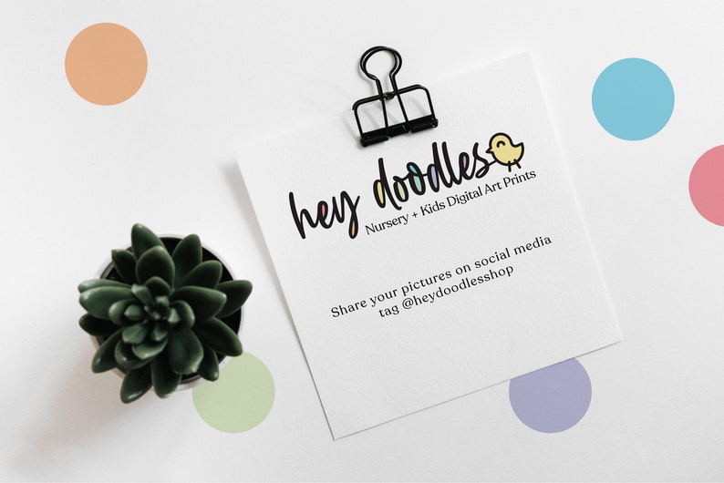 May include: A white card with the text "hey doodles" in colourful letters, a small yellow bird illustration, and the text "Nursery + Kids Digital Art Prints". Below the logo, the text reads "Share your pictures on social media tag @heydoodlesshop". The card is held by a black binder clip and is surrounded by colourful dots on a white background.