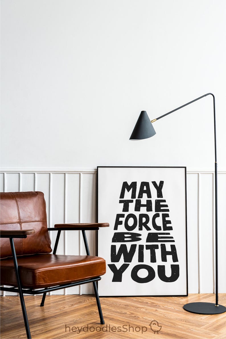 May include: Black and white typography print with the text "May the Force be with you" in a distressed font style. The print is framed and hanging on a white wall.