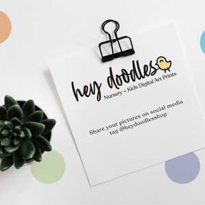 Op de afbeelding: Een witte kaart met zwarte tekst die "hey doodles Nursery + Kids Digital Art Prints Share your pictures on social media tag @heydoodlesshop" zegt. De kaart wordt vastgehouden door een zwarte paperclip. Een kleine potplant staat in de linkerbenedenhoek van de afbeelding. Er zijn kleurrijke stippen verspreid rond de kaart.