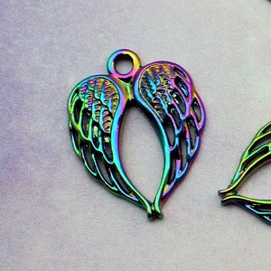 May include: A set of four iridescent metal angel wing charms. The wings are detailed with a delicate, intricate design and have a rainbow-like finish.