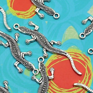 May include: A group of silver-toned lizard charms with textured details. The charms are scattered on a blue and yellow background with red circles.