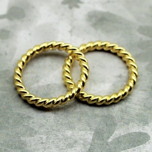 May include: Two gold-colored, twisted, metal rings. The rings are interlocked and are lying on a gray background.