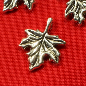 May include: Silver maple leaf charms on a red background. The charms are detailed and have a vintage look.