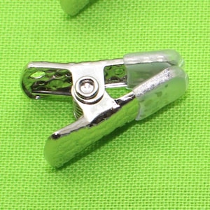 May include: Silver metal clip with a clear plastic top. The clip is designed for holding fabric or paper together.