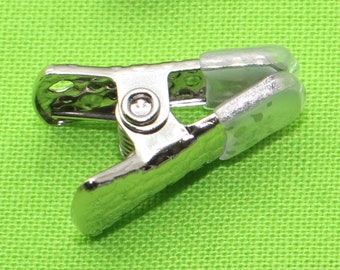 May include: Silver metal clip with a clear plastic top. The clip is designed for holding fabric or paper together.
