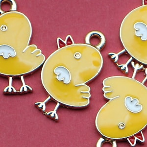 May include: Five gold-colored metal charms shaped like yellow chicks with red beaks and white wings. The charms have a loop at the top for attaching to a necklace or bracelet.