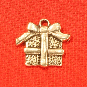 May include: A silver charm in the shape of a gift box with a bow on top. The charm has a textured surface and is perfect for adding to a bracelet or necklace.