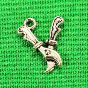 May include: Silver charm in the shape of a pair of pruning shears. The charm is on a green fabric background.