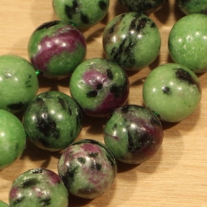 May include: A strand of green, black, and pink gemstone beads. The beads are round and have a smooth, polished finish.
