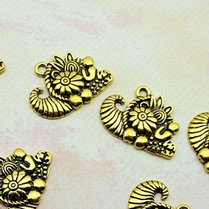 May include: A collection of eight gold-toned metal charms shaped like a cornucopia, each with intricate floral designs and a loop for attaching to jewelry or other crafts.