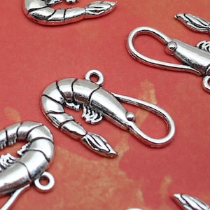 May include: Silver charm pendants shaped like shrimp, with a loop at the top for attaching to jewelry. The charms are detailed with realistic features, including the shrimp's legs, tail, and antennae.