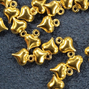 May include: A scattering of gold-colored metal heart-shaped charms with a loop at the top. The charms are on a dark blue background.