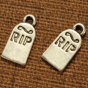 May include: Two silver-toned metal charms shaped like tombstones with the word "RIP" engraved on them.