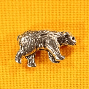 May include: A silver bear charm with a detailed design. The bear is walking on all fours and has a slightly raised head.