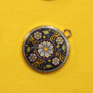 May include: Five round, gold-toned pendants with a floral design. The pendants feature a white flower with a yellow center surrounded by green leaves and a dark blue background.
