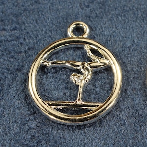 May include: Two silver-toned metal charms in the shape of a circle with a gymnast performing on a balance beam inside.