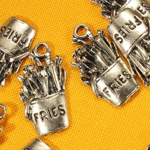 May include: A collection of silver-toned metal charms shaped like french fries in a paper container. Each charm has the word "FRIES" printed on it.