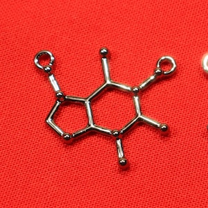 May include: Two silver charms shaped like the chemical structure of caffeine. The charms are on a red background.