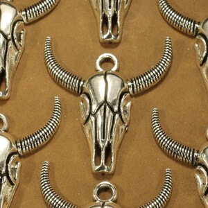 May include: A collection of silver-toned metal charms shaped like bull skulls. Each charm has intricate details and a loop for attaching to a necklace or bracelet.