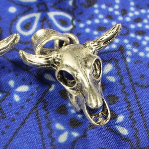 May include: Three silver bull skull charms with intricate details. The charms are on a blue bandana background.