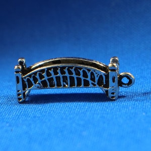 May include: Two silver bridge charms with a detailed design. The charms are small and have a loop for attaching to a bracelet or necklace.