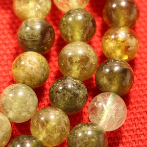 May include: A strand of green and yellow gemstone beads. The beads are round and have a smooth, polished finish. The beads are strung on a clear cord.