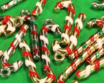 May include: A collection of gold and silver candy cane charms with red and white stripes and green accents. The charms are scattered on a green surface.