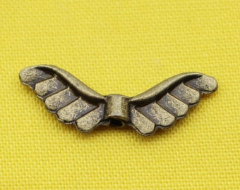 May include: A pair of antique gold-toned metal wings with a decorative design. The wings are connected in the center with a small metal loop.