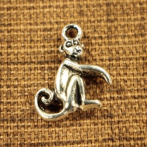 May include: Silver charm in the shape of a monkey sitting with its tail curled around its legs.