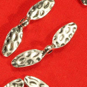 May include: Two silver propeller-shaped charms with a textured surface. The charms have a loop at the top for attaching to jewellery or other crafts.