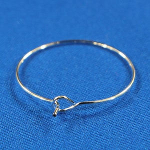 May include: A silver bangle bracelet with a simple, circular design and a small, looped clasp.
