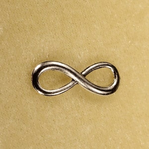 May include: A silver infinity symbol charm on a beige background.