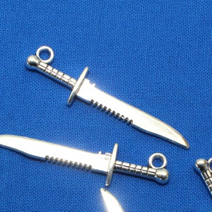 May include: Three silver-toned metal knife charms with a serrated edge and a ring at the top for attaching to a keychain or bracelet.