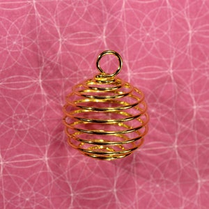 May include: A gold metal wire cage pendant, designed to hold crystals or other small objects. The cage is oval-shaped and has a loop at the top for hanging.