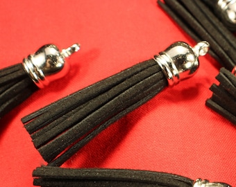 May include: Close-up of black suede tassels with silver metal caps. The tassels are arranged on a red fabric surface.